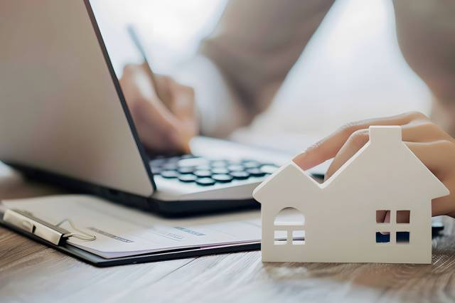 Person bearbeitet Akten, Modell eines Hauses im Vordergrund